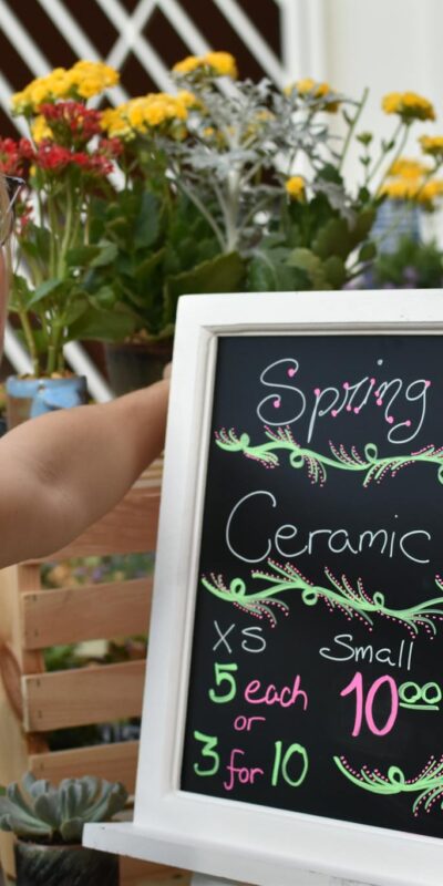 A woman arranging flowers at a ceramic fundraiser, featuring spring blooms and a pricing sign.