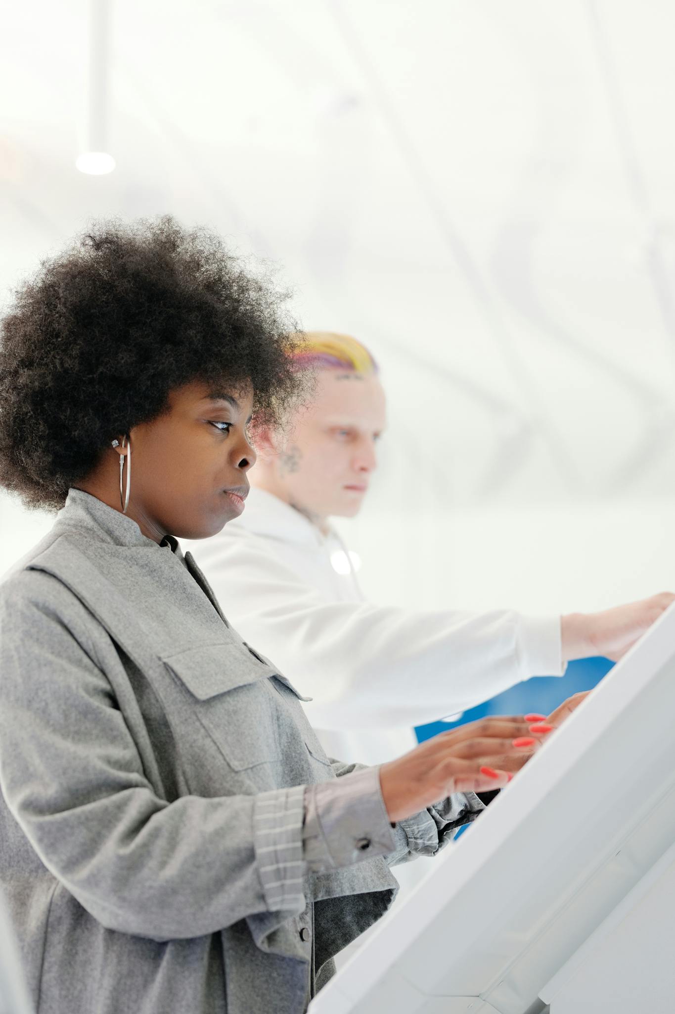 Side view of a stylish woman with afro hair using a touchscreen indoors.